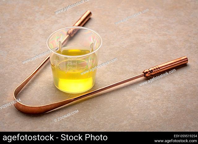 measuring cup of pulling oil and a copper tongue scrapper, oral hygiene concept