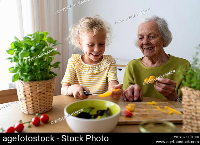 Smiling grandmother and granddaughter examining vegetables on table