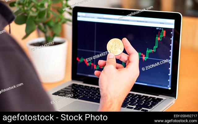 man checking cryptocurrency chart and bitcoin coins on a laptop