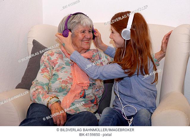 Granddaughter and grandmother listening to music through headphones, digital music, Bavaria, Germany