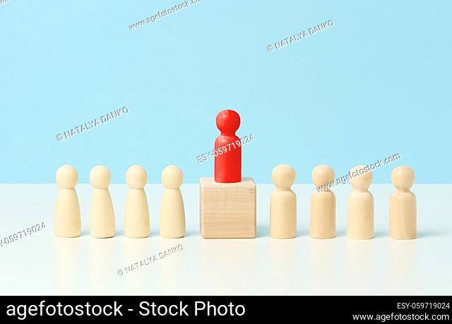wooden little men on a white table, red stands on a wooden cube. Search for talented employees, rally, manipulation of the masses