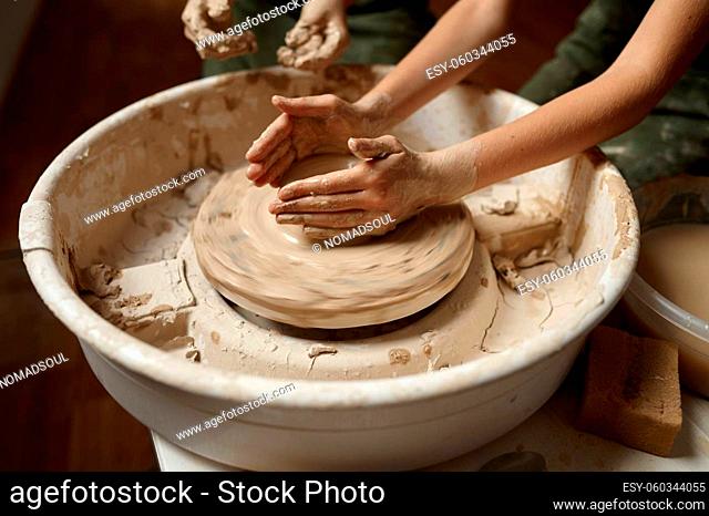 Children work on a potter's wheel in the workshop, top view on hands. Clay modeling lesson at the art school. Young masters of folk crafts, pleasant hobby