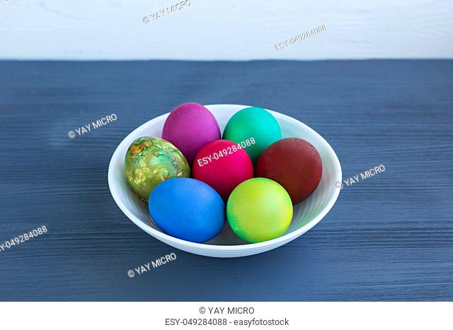 White plate of Easter multicolored boiled eggs decoration on grey wooden background