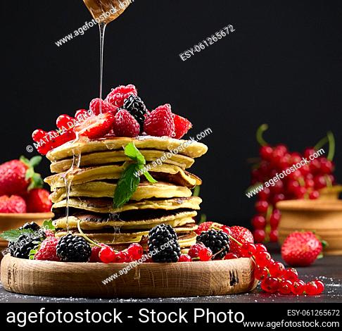 Stack of pancakes with fresh fruit sprinkled with honey on a black background