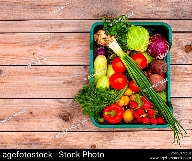Top view of a set of different vegetables stacked in a basket on the wooden background with copyspace on the left side