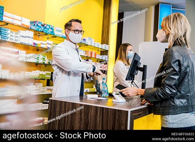 Female customer wearing face mask while making payment through smart phone at checkout counter in pharmacy