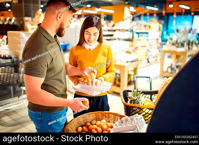 Family couple choosing eggs in grocery store. Man and woman with cart buying beverages and products in market, two customers shopping food and drinks