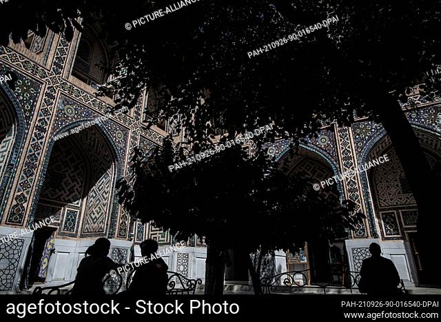 26 September 2021, Uzbekistan, Samarkand: Uzbeks sit under a tree in the historical landmark of Registan in Samarkand. The Registan was a public square and...
