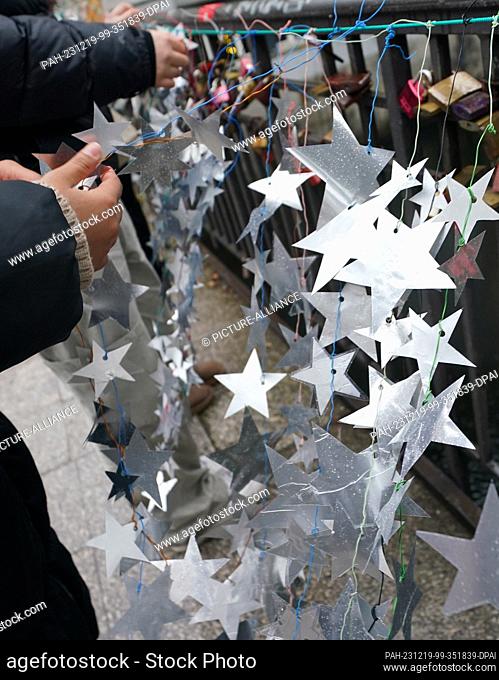 19 December 2023, Hamburg: Schoolgirls attach homemade stars made from the aluminum lids of yogurt and pudding cups to the Michaelis Bridge in the city center