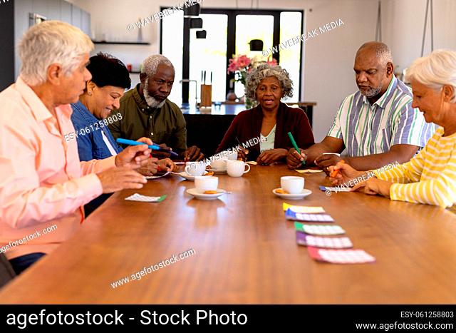 Multiracial senior friends playing bingo while having coffee and cookies at dining table