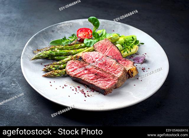Barbecue dry aged wagyu entrecote beef steak with lettuce and green asparagus as closeup on a modern design plate