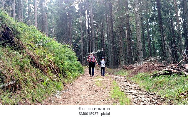 Mother and son climb the mountain road up hill holding hand Woman with backpack and child walking in forest nature