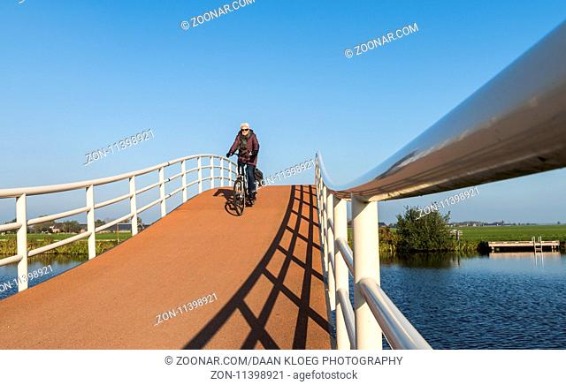 Groot-Ammers, The Netherlands - November 11, 2016: Modern architecture of a cycling bridge over a small canal with three cyclists at Groot-Ammers in the...