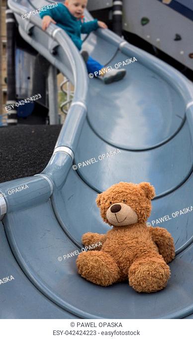Teddy bear going down on a slide followed by a little Caucasian boy in an outdoor playground