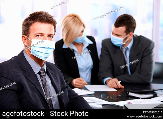 Businessman fearing h1n1 swine flu virus wearing protective face mask during meeting at office