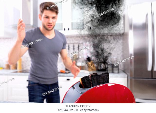 Frustrated Young Man Looking At Burnt Toasts In Toaster At Kitchen