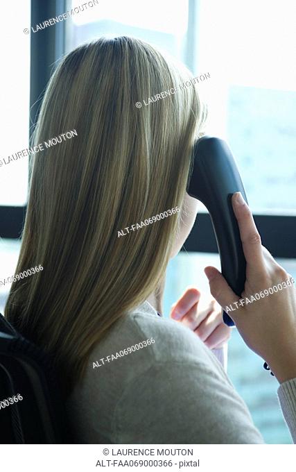 Woman looking out window while talking on landline phone, rear view