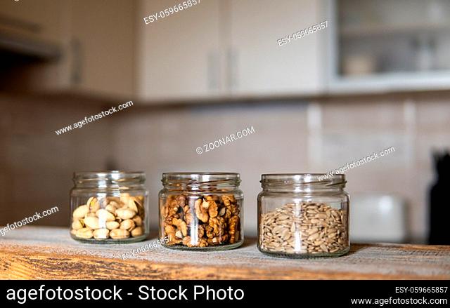 Sunflower seeds, walnut and almond in a jars which standing on a white vintage table with a kitchen on background. Nuts is a healthy vegetarian protein and...