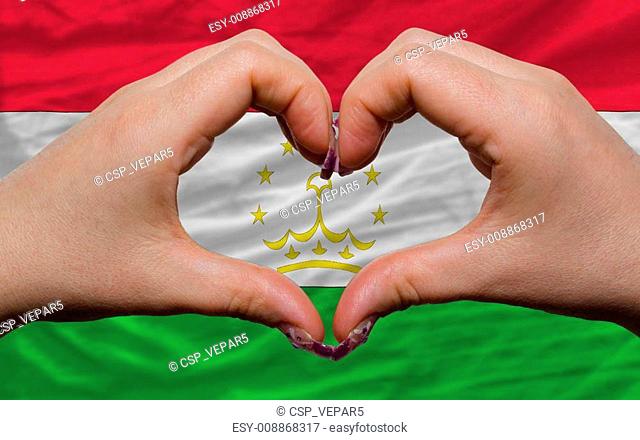 Gesture made by hands showing symbol of heart and love over national tajikistan flag