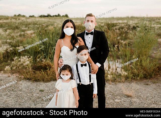 Parents and children in wedding dress wearing face mask while standing in field during COVID-19