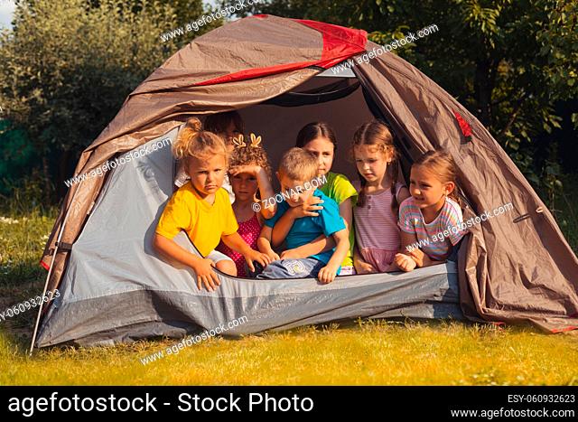 The little kids look out of the tent. They rest in the garden on a summer day