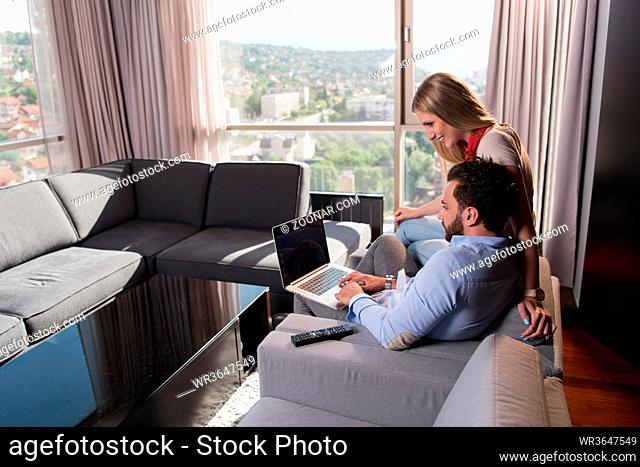 Young couple relaxing at home using laptop computers reading in the living room near the window on the sofa couch