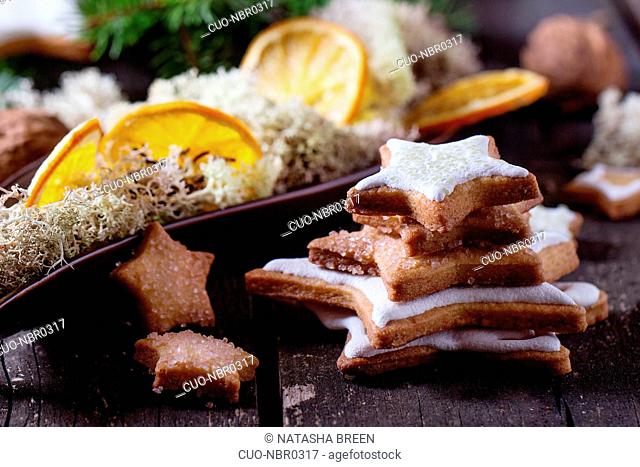 Christmas glazed star shapes cookies with Christmas tree, moss and dry sliced orange in ceramic plate over red wooden table. Dark rustic style