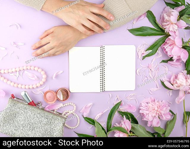 two hands with smooth skin of a young girl and a handbag with cosmetics, bouquet of blooming pink peonies, fashionable concept, top view