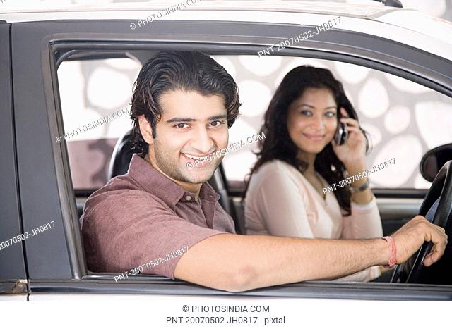 Portrait of a young man driving a car with a young woman talking on a mobile phone