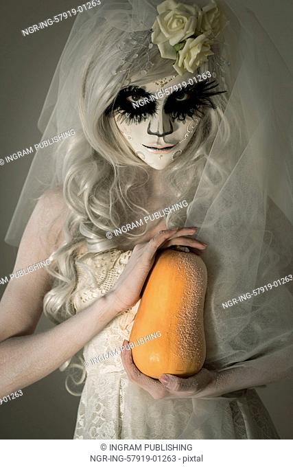 Halloween witch. Beautiful woman wearing santa muerte mask holding pumpkin