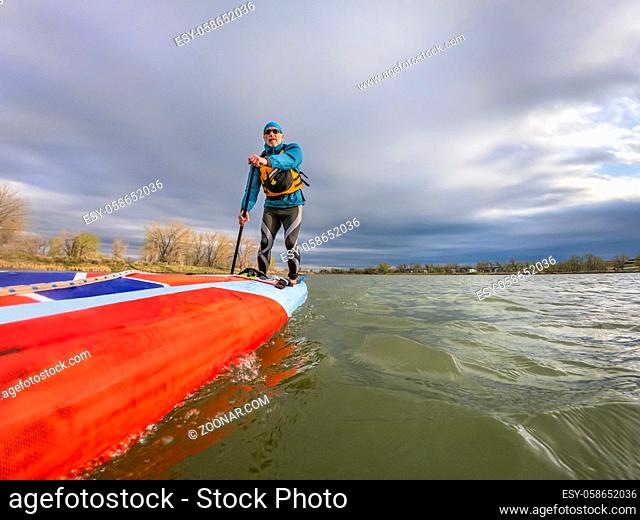 Low angle view from action camera of a senior male paddler on a long racing stand up paddleboard on a lake in Colorado. Recreation, training and fitness concept