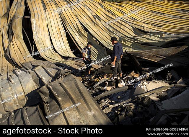 10 September 2020, Greece, Moria: Two men are standing in the burnt-out refugee camp Moria between corrugated sheets that were deformed by the fire
