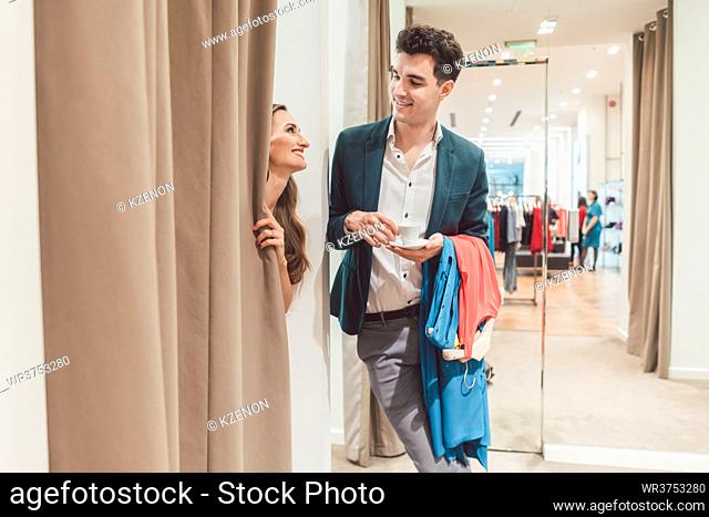 Man in fashion store waiting for his woman to appear from the fitting room being a bit bored