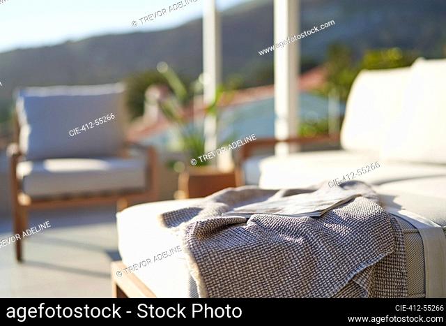 Blanket and magazine on sunny patio sofa