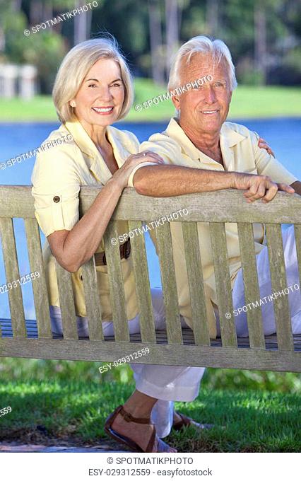 Happy romantic senior couple sitting on a park bench next to a blue lake