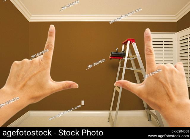 Hands framing brown painted room wall interior with ladder, paint bucket and rollers