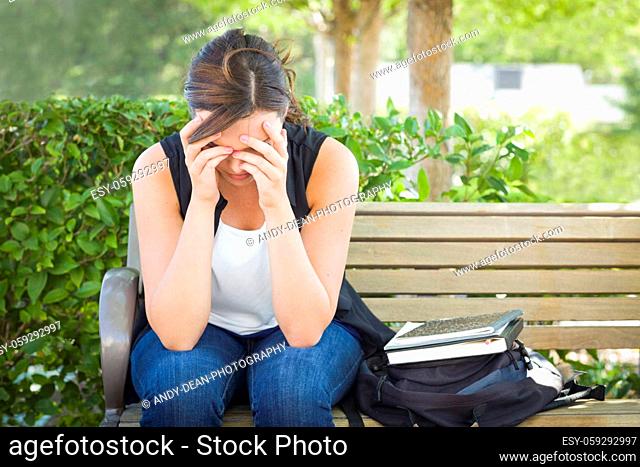 Upset Young Woman Sitting Alone with Her Head in Her Hands on Bench Next to Books and Backpack