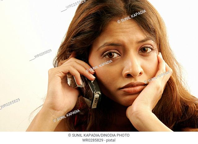 South Asian Indian teenager girl wearing red colour contact lenses in eyes disappointingly talking on mobile phone MR686G