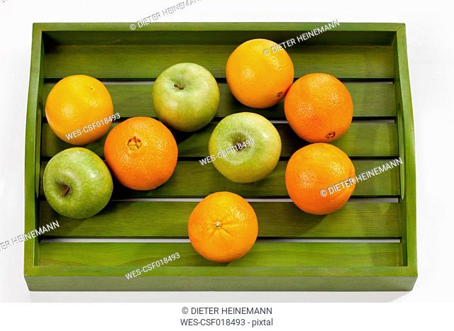 Green apples and oranges on wooden tray, close up