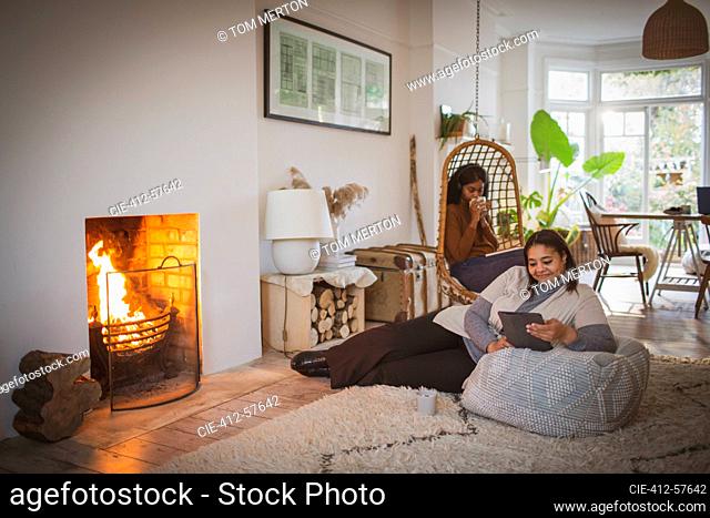 Madre e hija relajándose con tableta digital y libro junto a la chimenea