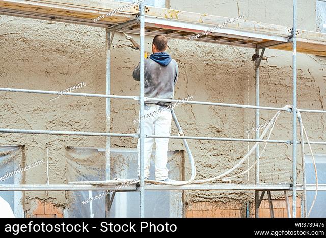Construction worker plastering outer wall of newly built house
