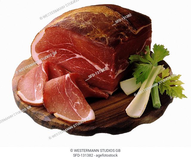 Piece of raw ham and two slices on board with celery