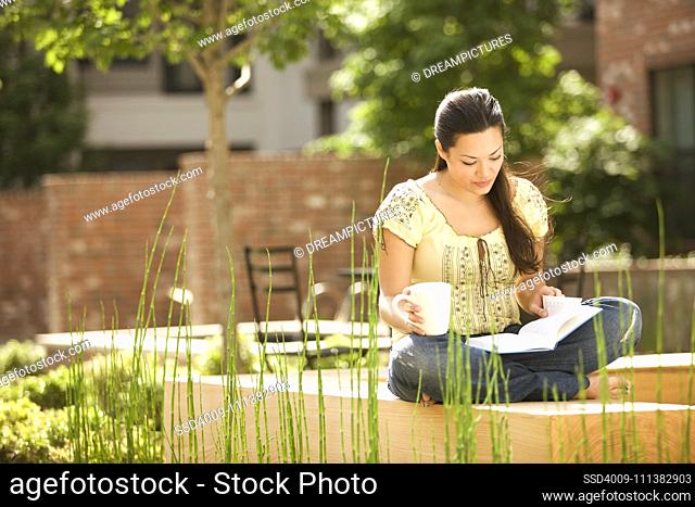 Mixed race woman reading book and holding coffee cup outdoors
