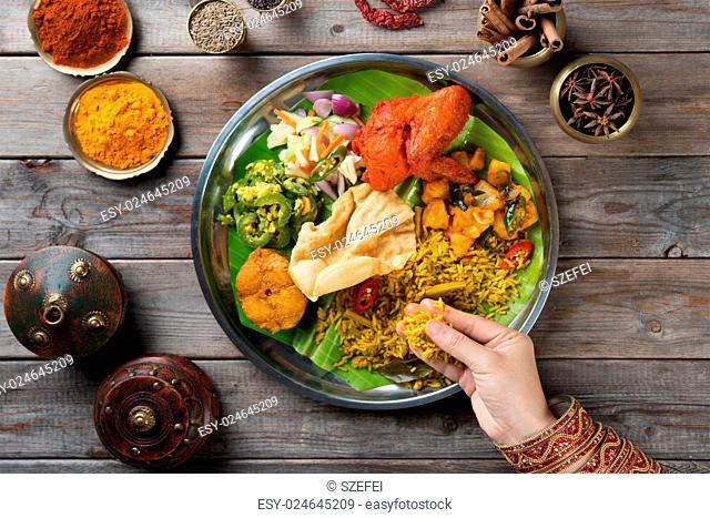 Overhead view of Indian woman's hand eating biryani rice on wooden dining table
