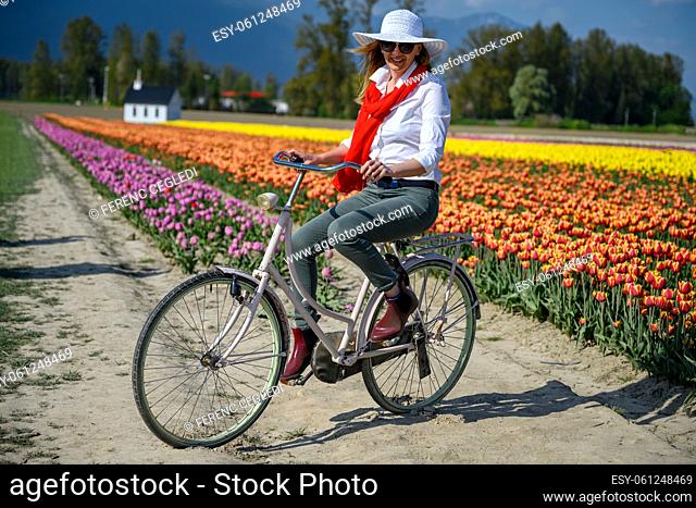 Very happy, very excited caucasian woman riding her old bike by the tulip field. Arms and legs wide open and she shows happiness in British Columbia, Canada