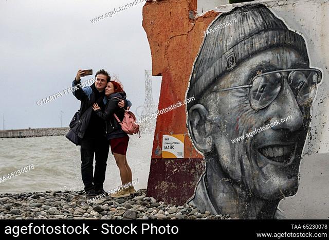RUSSIA, SOCHI - NOVEMBER 26, 2023: A couple take a photograph by a Jacques-Yves Cousteau mural on a beach as high winds and waves hit the resort of Sochi during...