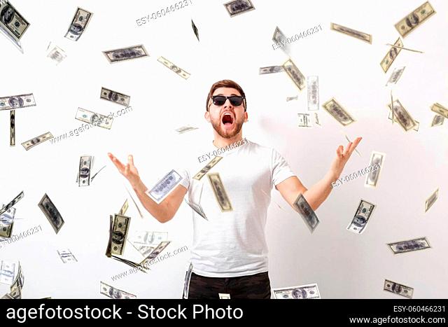 young handsome happy man with a beard in a white shirt standing under money rain of dollar bills