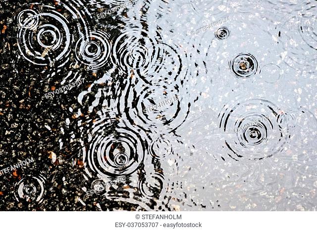 Rain on asphalt or tarmac road creating ripples, high contrast during autumn
