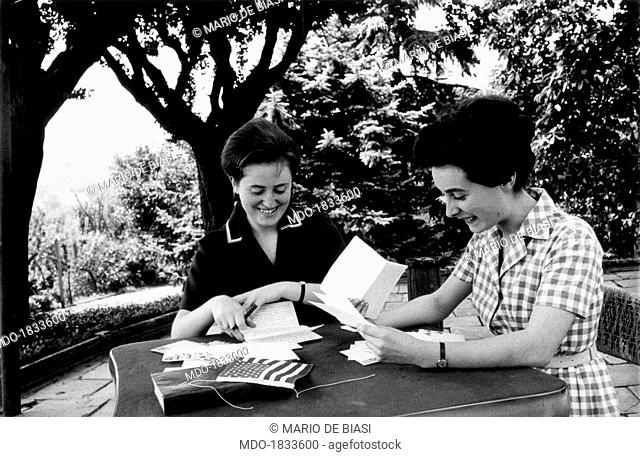 Isa Signorini, on the left, and Lina Manera, two students of the Istituto Tecnico Commerciale of Alba, sitting at a table in a patio in the middle of a garden;...