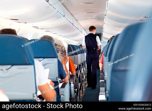 Interior of airplane with passengers on seats and steward walking the aisle